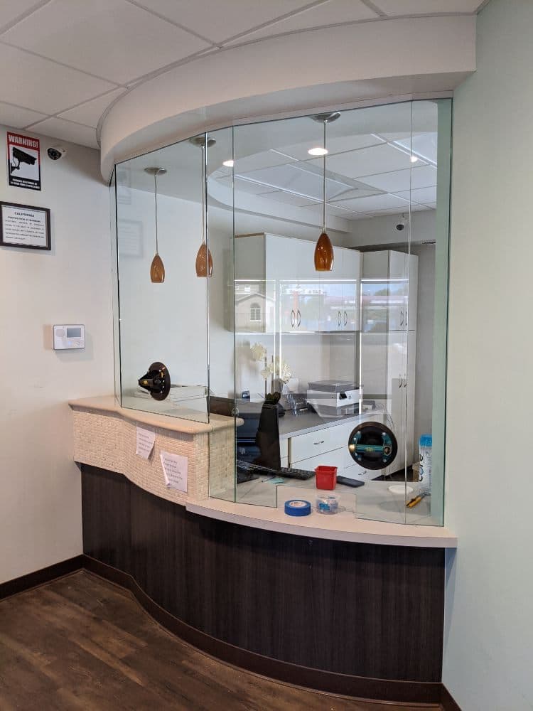 Curved frameless glass screen set above a reception counter in an office