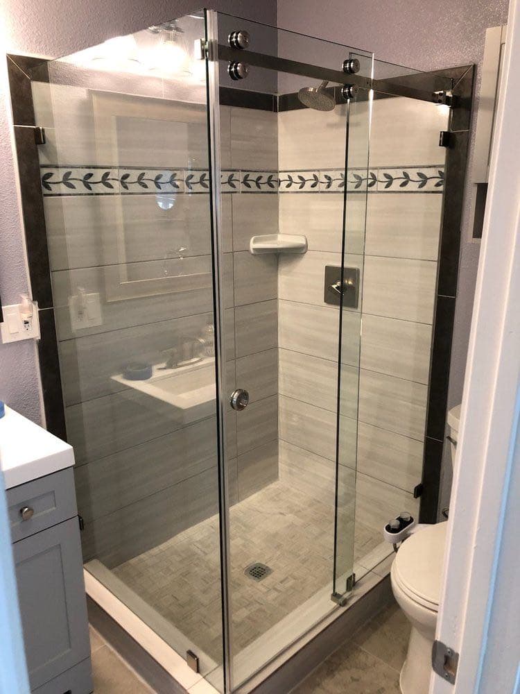 Frameless glass shower enclosure with brushed-nickel hinges and clamps, in a bathroom tiled in pale grey