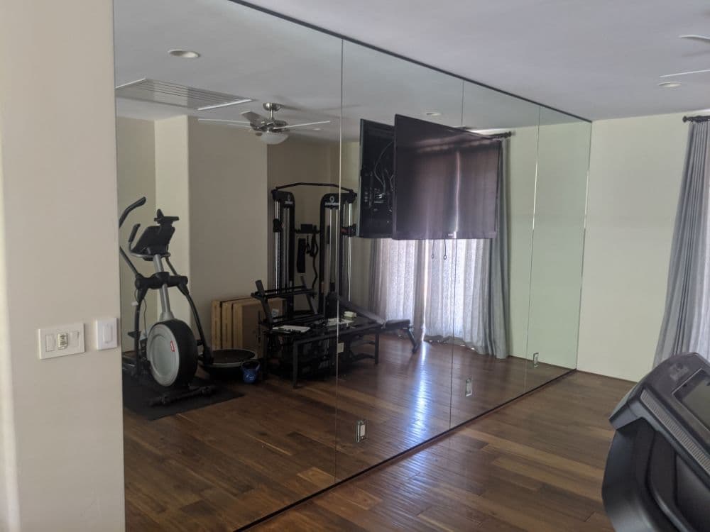 Full-height wall mirror in a home gym, reflecting an elliptical trainer, a weight machine and a wall-mounted television