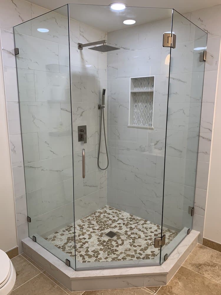 Neo-angle frameless shower enclosure with brushed nickel clamps against marble-look tile